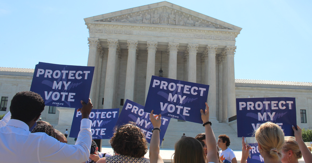 Six people hold up blue signs that read 'protect my vote' at a rally in front of the supreme court