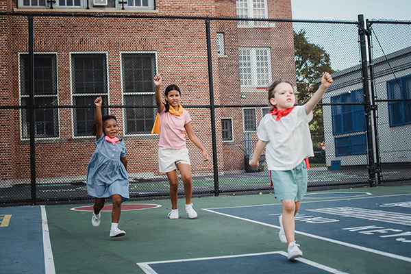 Three children playing on a basketball court pretending to be superheroes.