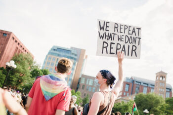 Protestors hold a sign that reads "We repeat what we don't repair."